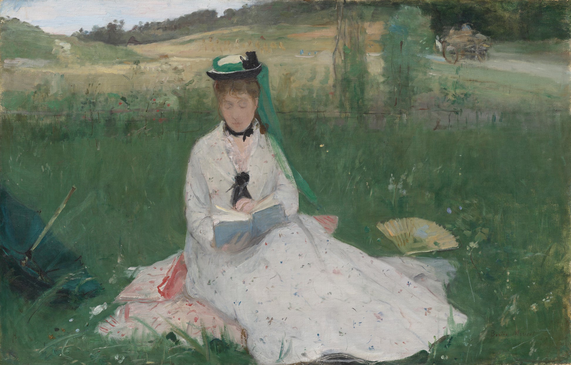 Woman in a white dress sitting on grass reading a book, with a landscape in the background