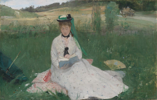 Woman in a white dress sitting on grass reading a book, with a landscape in the background