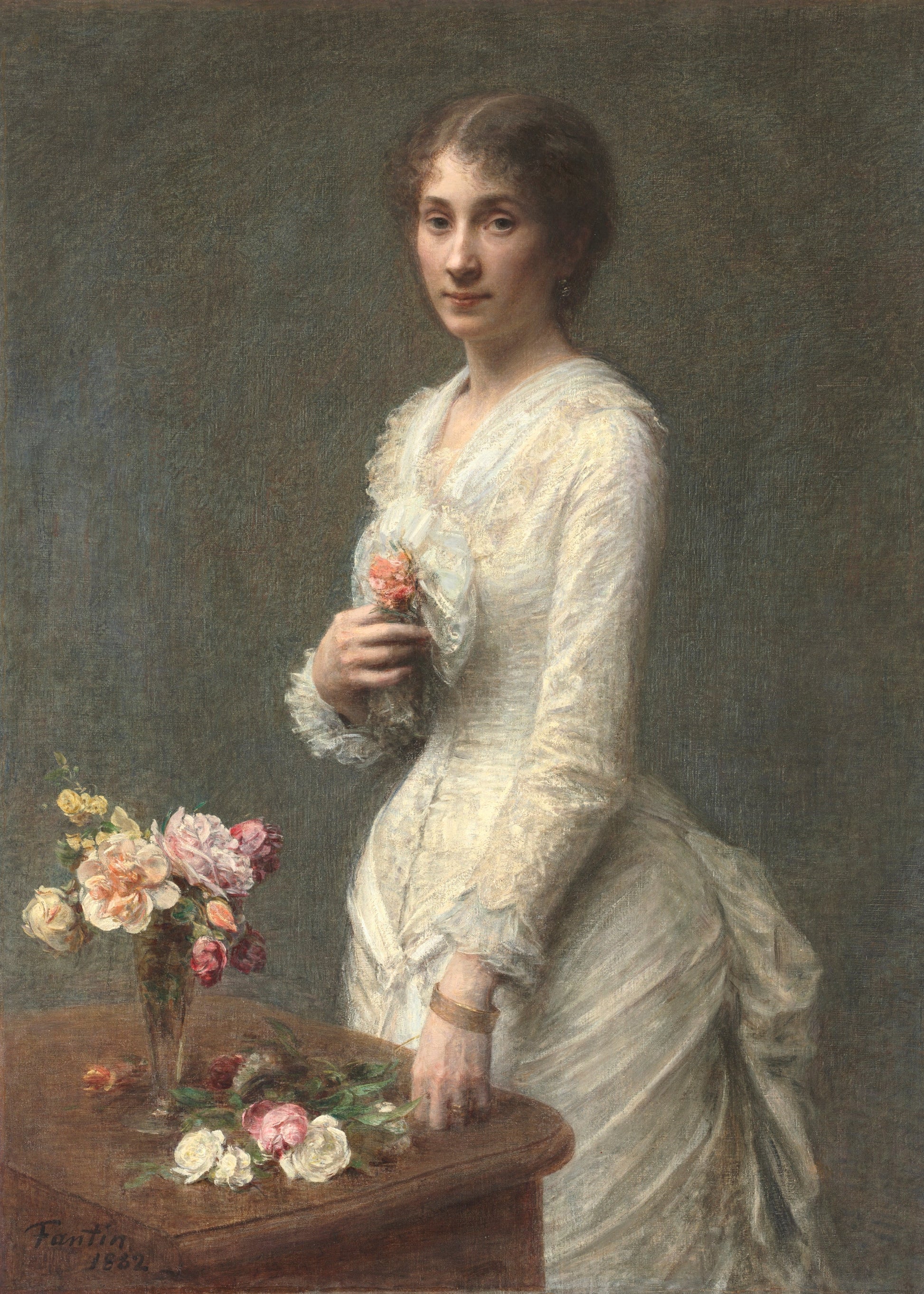 Portrait of a woman in a white dress holding flowers, with a vase of flowers on a table in front of her.