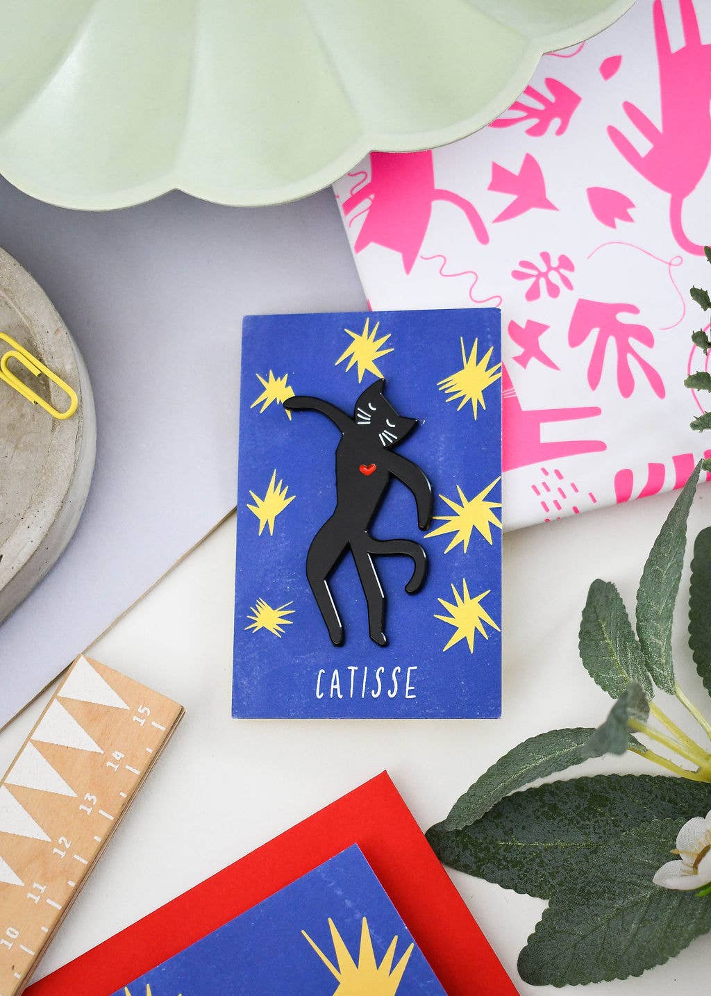 Blue card with a black figure and 'Catisse' text, surrounded by colorful cards and plants.