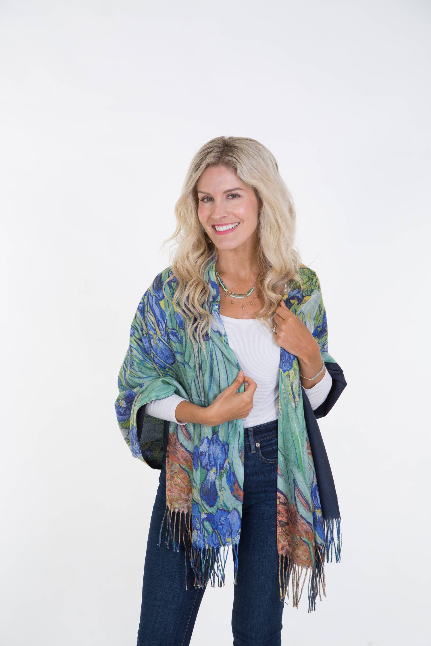A woman smiling and presenting a multicolored scarf with a floral pattern, draped around her neck and shoulders.