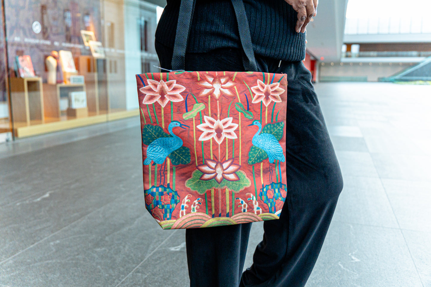 Person holding a tote bag with floral and bird design in an indoor setting