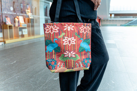 Person holding a tote bag with floral and bird design in an indoor setting
