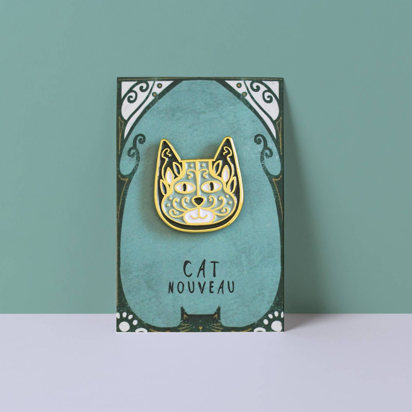 Gold cat-shaped pin on a teal card with 'Cat Nouveau' text against a teal background