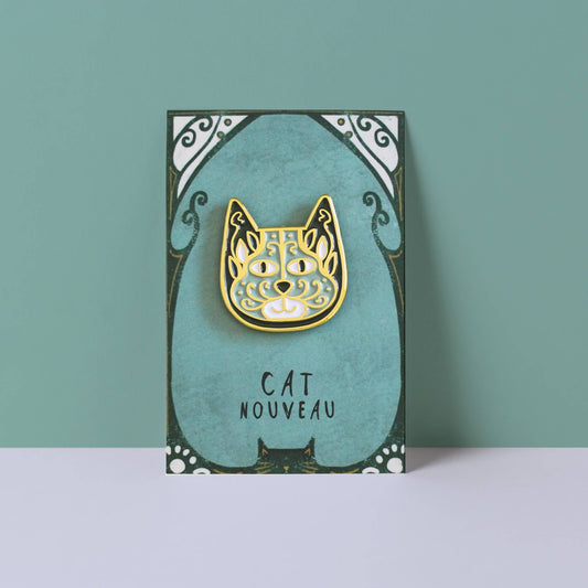 Gold cat-shaped pin on a teal card with 'Cat Nouveau' text against a teal background